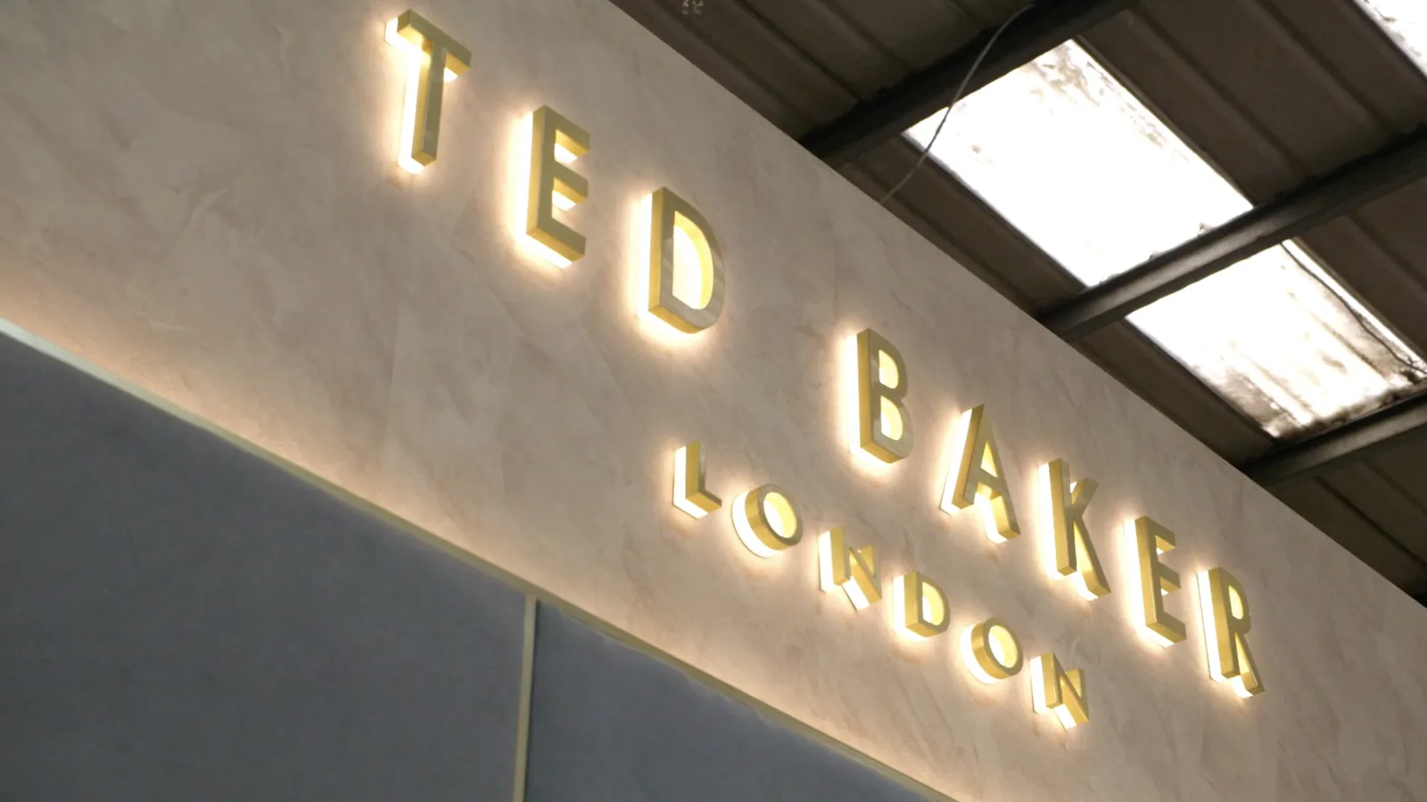 Backlit brass Ted Baker London lettering on a stone-effect wall.