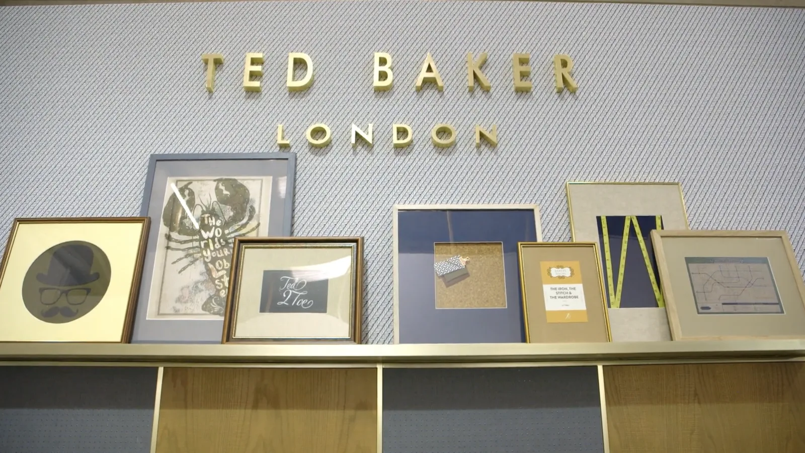 A finished display wall with Ted Baker London lettering above a shelf of framed prints.