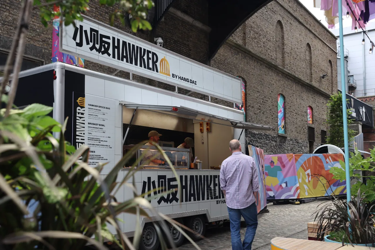 The Hawker by Hang Dai food truck in the Cobble Yard, with a brick arch and painted hoardings behind it.